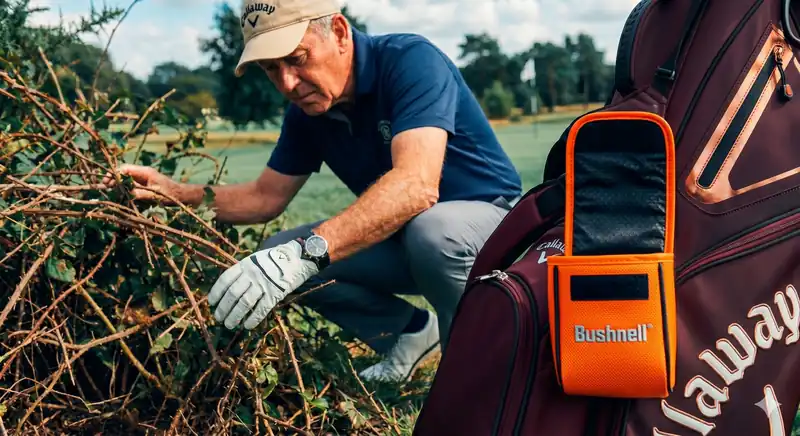 Rangefinder am Golfbag, während ein Golfer im Gebüsch nach verlorenem Zubehör sucht